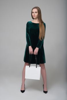 Young beautiful long-haired girl in dark green dress poses with white paper bag for shopping