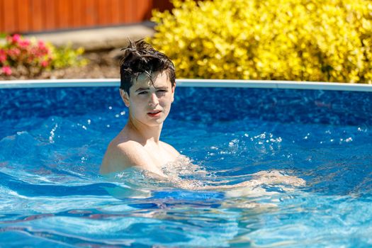 Young teenager boy in the garden swimming pool in spring time