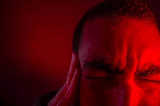 Man is suffering in pain from headache. Close up headshot portrait of man feeling upset or in pain. He touches his head with his hand.