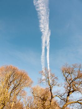 two white trails in the blue sky with trees from plane; essex; england; uk