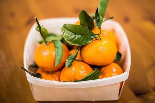 A bowl of mandarin oranges with green stalks and leaves.