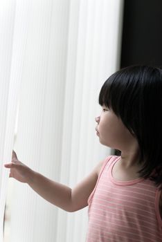 Sad little Asian girl looking at window