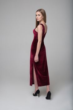 Young beautiful long-haired female model poses in long red dress on grey background