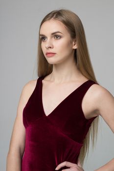 Young beautiful long-haired female model poses in red dress on grey background
