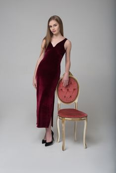 Young long-haired girl poses in long red dress near chair