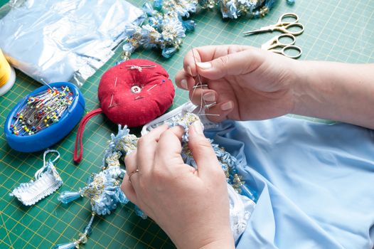 A woman sews a decorative element to clothes with a needle