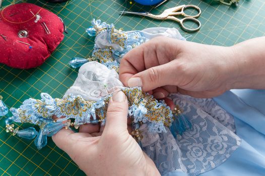 A woman sews a decorative element to clothes with a needle