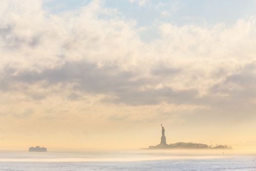 Staten Island Ferry cruises past the Statue of Liberty on a misty sunset. Manhattan, New York City, United States of America. Vertical composition. Copy space.