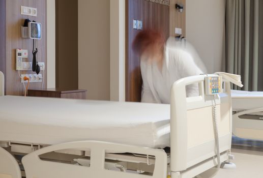 A blurred figure of a sanitarian taking care of a modern hospital beds.