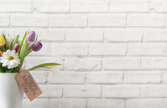 Selection of tulips and daisies inside a pot on top of a fireplace mantelpiece with label