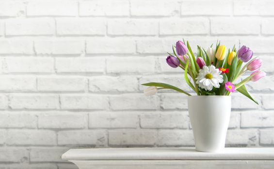 Selection of spring flowers inside a pot on top of a fireplace mantelpiece 
