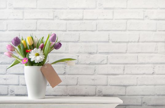 Selection of tulips and daisies inside a pot on top of a fireplace mantelpiece with label