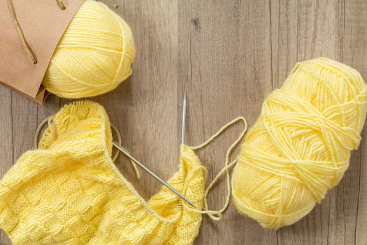 Light yellow knitting wool and knitting needles on wooden background. Top view.copy space. Knitted fabric and yarn on a wooden surface.