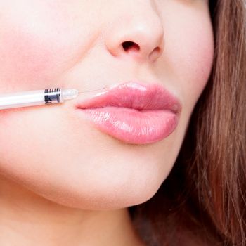 Closeup shot of beautiful female lips and syringe with filler.