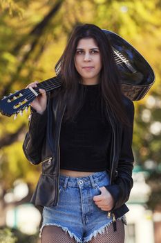 Close view of a beautiful young woman with classic guitar on a garden in the city.