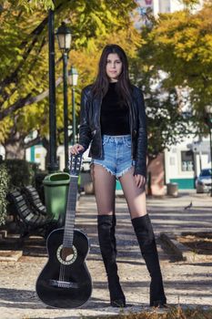 Close view of a beautiful young woman with classic guitar on a garden in the city.