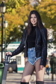 Close view of a beautiful young woman with classic guitar on a garden in the city.