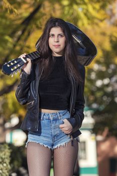 Close view of a beautiful young woman with classic guitar on a garden in the city.