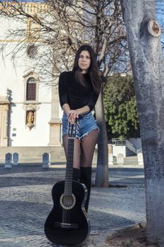 Close view of a beautiful young woman with classic guitar on the streets of the city.