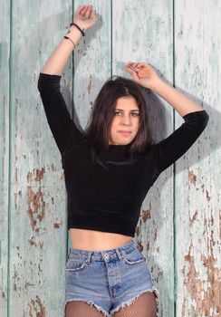 Close view of a beautiful young woman with short blue jeans over a green wooden background.