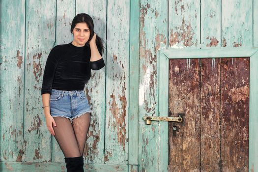 Close view of a beautiful young woman with short blue jeans over a green wooden background.