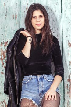 Close view of a beautiful young woman with short blue jeans over a green wooden background.