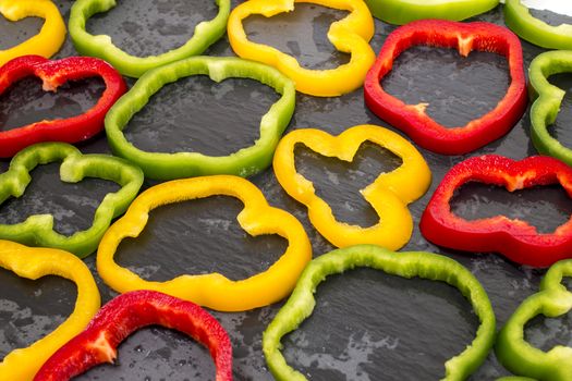 colorful sliced bell peppers on a black stone of schist, wet and organized.