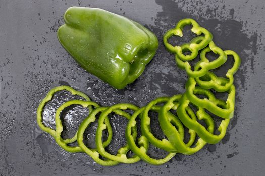 green bell peppers on a black stone of schist, wet and sliced.