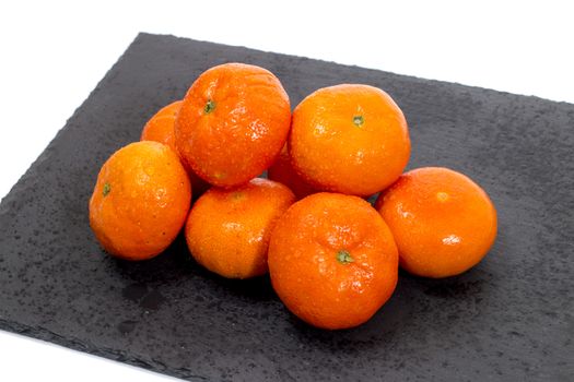 Wet clementines fruits on a black slab of schist.