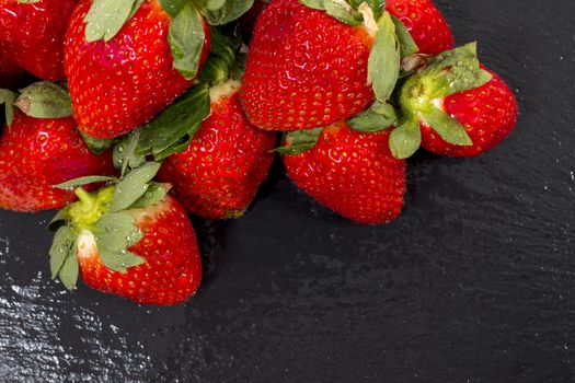 Red tasty strawberries on a black slab of schist.