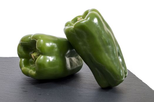 two green bell peppers on a black stone of schist.