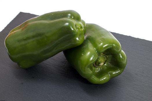 two green bell peppers on a black stone of schist.