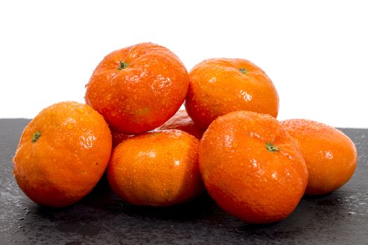 Wet clementines fruits on a black slab of schist.