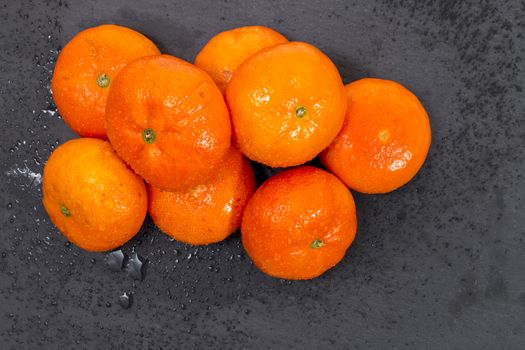 Wet clementines fruits on a black slab of schist.