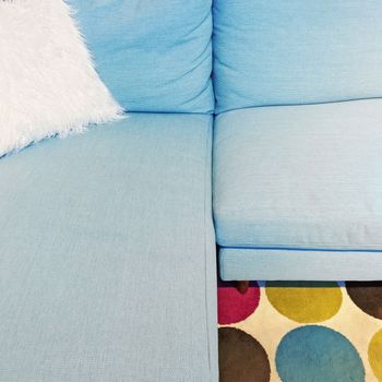 Fluffy white cushion on a blue textile sofa. Modern furniture with retro feel.