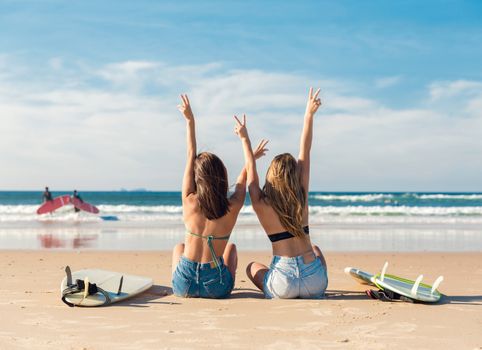 Two beautiful surfer girls at the beach with arms open