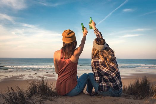 Two best friends sitting on the coastline toasting to friendship