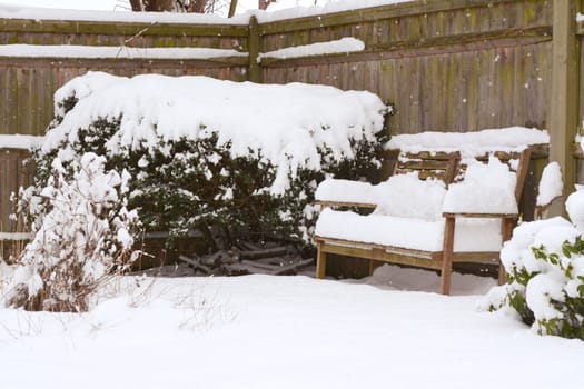 Deep snow on a wooden bench and shrubs and plants in a country garden 