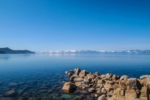 Scenic view of beautiful Lake Tahoe in Spring, landscape of the United States of America, clear water, nice sky, stone island, tree, fresh air and snow mountains