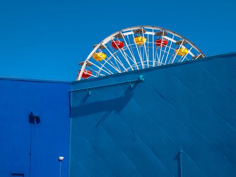 Colorful Ferris wheel behind blue wall at Santa Monica beach