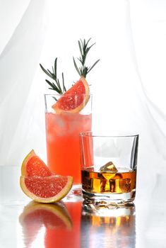 Paloma cocktail in Collins Glass, from tequila with grapefruit juice, decorated with a slice of grapefruit and rosemary.Whiskey in rocks glass with  ice cubes . Drinks  on a light background.