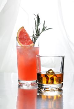 Paloma cocktail in Collins Glass, from tequila with grapefruit juice, decorated with a slice of grapefruit and rosemary.Whiskey in rocks glass with  ice cubes . Drinks  on a light background.