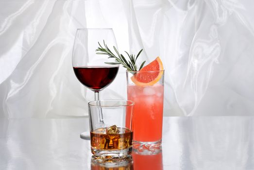 Paloma cocktail in Collins Glass, Whiskey in rocks glass with  ice cubes, red wine in Bordeaux-shaped glass. Drinks  on a light background.