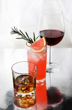 Paloma cocktail in Collins Glass, Whiskey in rocks glass with  ice cubes, red wine in Bordeaux-shaped glass. Drinks  on a light background.