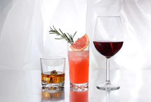 Paloma cocktail in Collins Glass, Whiskey in rocks glass with  ice cubes, red wine in Bordeaux-shaped glass. Drinks  on a light background.