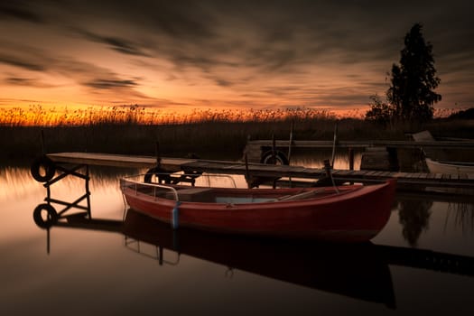 Red rowing boat attached to dock. Very beautiful sunset.