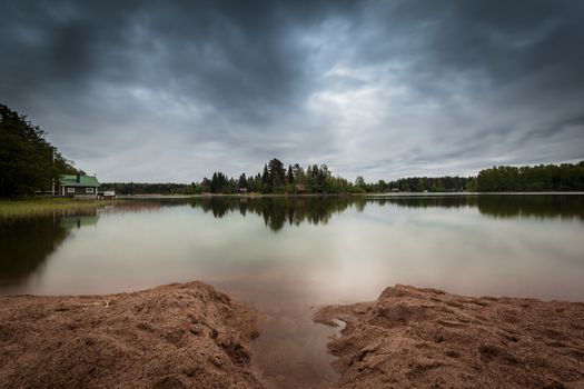 A tranquil landscape picture where the storm is coming. Clear reflection on the surface of the water.