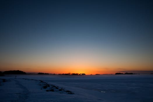 Sunset landscape in cold winter weather. Frozen sea and islands.