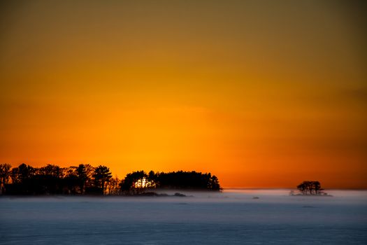 The sun goes down behind the trees in Luvia, Finland. There is also a slight fog on the ice surface.