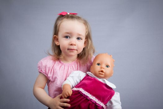 Portrait of the cute girl with a doll. Gray background.